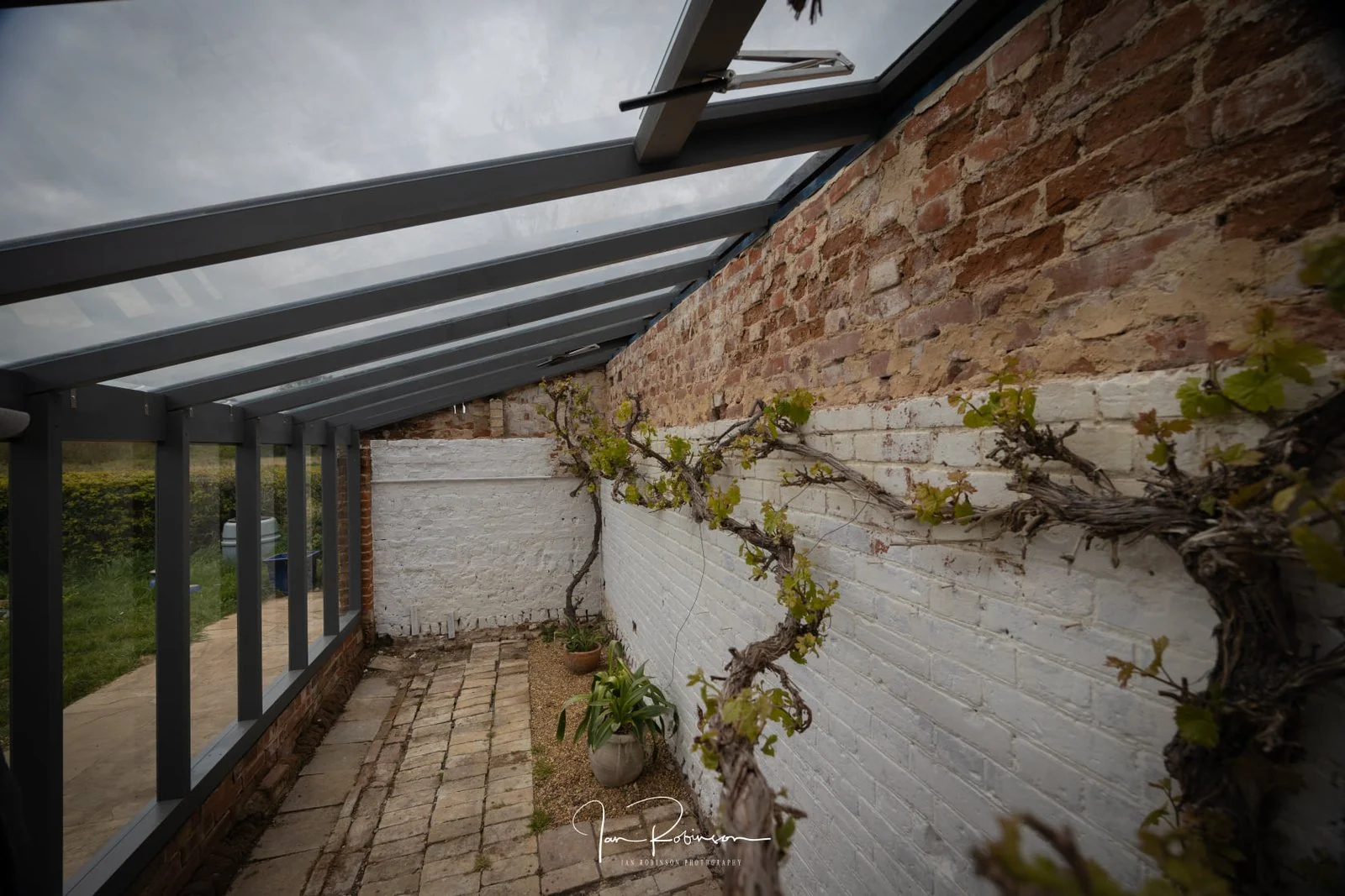 Interior of greenhouse with timber framing against historic brick wall